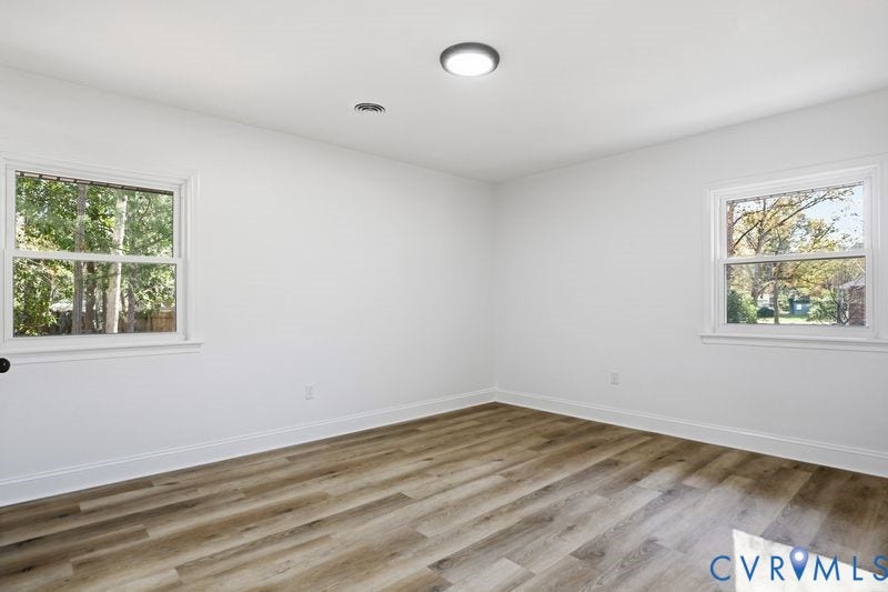 Neutral interior featuring wood-finish flooring, two double-hung windows, and flush-mount ceiling lighting