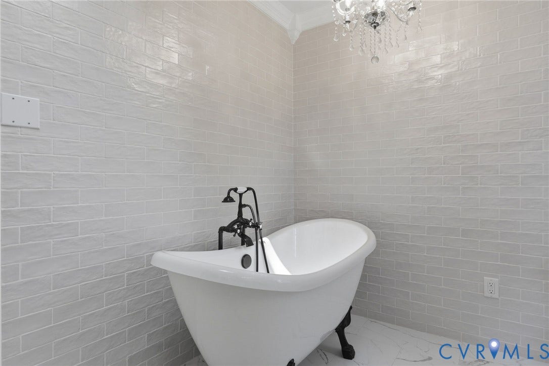 2311 Castle Hill Road, Midlothian, VA 23113 Freestanding clawfoot tub featuring a black faucet assembly, floor-to-ceiling textured tile wall, crown molding, and crystal chandelier