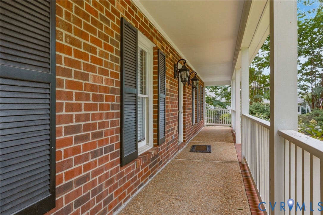 2311 Castle Hill Road, Midlothian, VA 23113 Covered front porch featuring red brick exterior wall, dark louvered shutters, exposed aggregate concrete flooring, and metal carriage-style wall lanterns