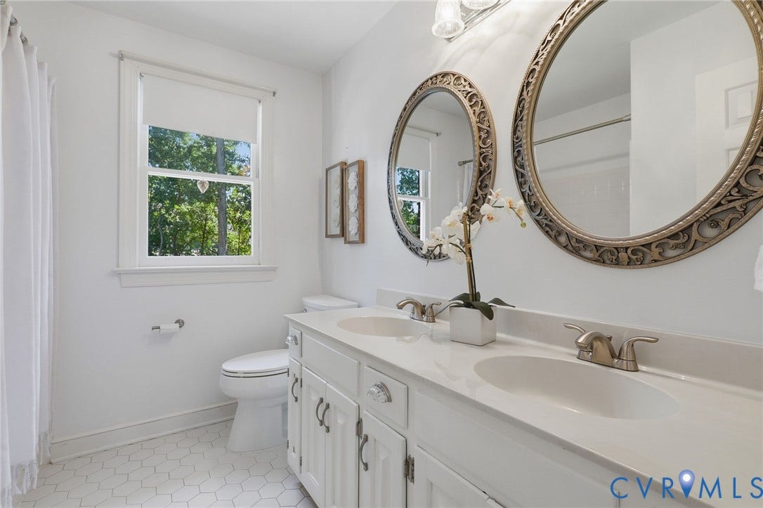 2311 Castle Hill Road, Midlothian, VA 23113 Dual-sink vanity with white cabinetry and integrated stone-top surface, white hexagonal floor tile, and double oval wall-mounted mirrors