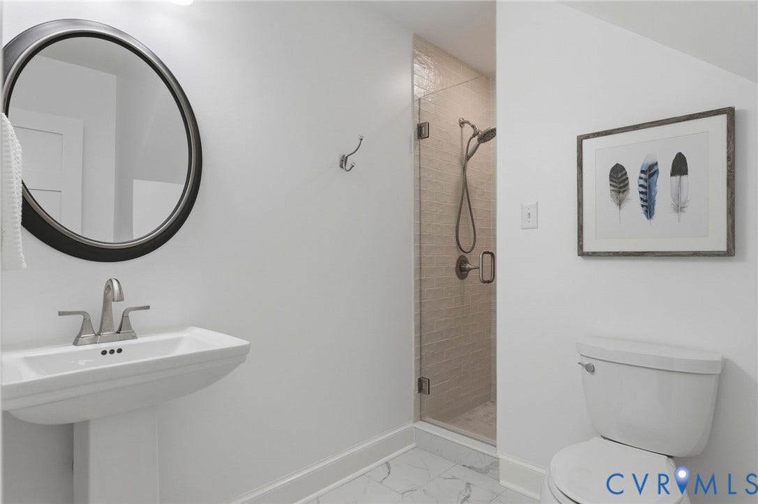2311 Castle Hill Road, Midlothian, VA 23113 Bathroom featuring a pedestal sink, circular wall-mounted mirror, walk-in shower with a glass door and tiled surround, and stone-finish flooring