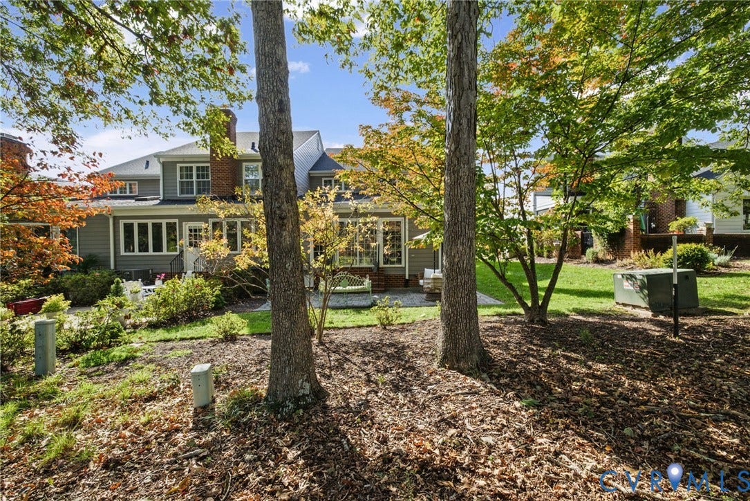 13908 Pagehurst Terrace, Salisbury, Midlothian, VA 23113 Rear exterior featuring gray horizontal siding, a brick chimney, a stone patio, and mature trees on a lawn