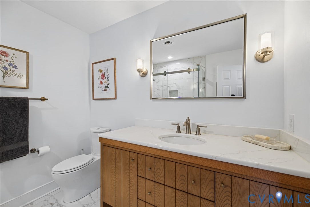 13908 Pagehurst Terrace, Salisbury, Midlothian, VA 23113 Bathroom featuring a wood-finish vanity with a stone-composite countertop, undermount sink, metallic-finish wall sconces, a framed mirror, and a two-piece elongated toilet