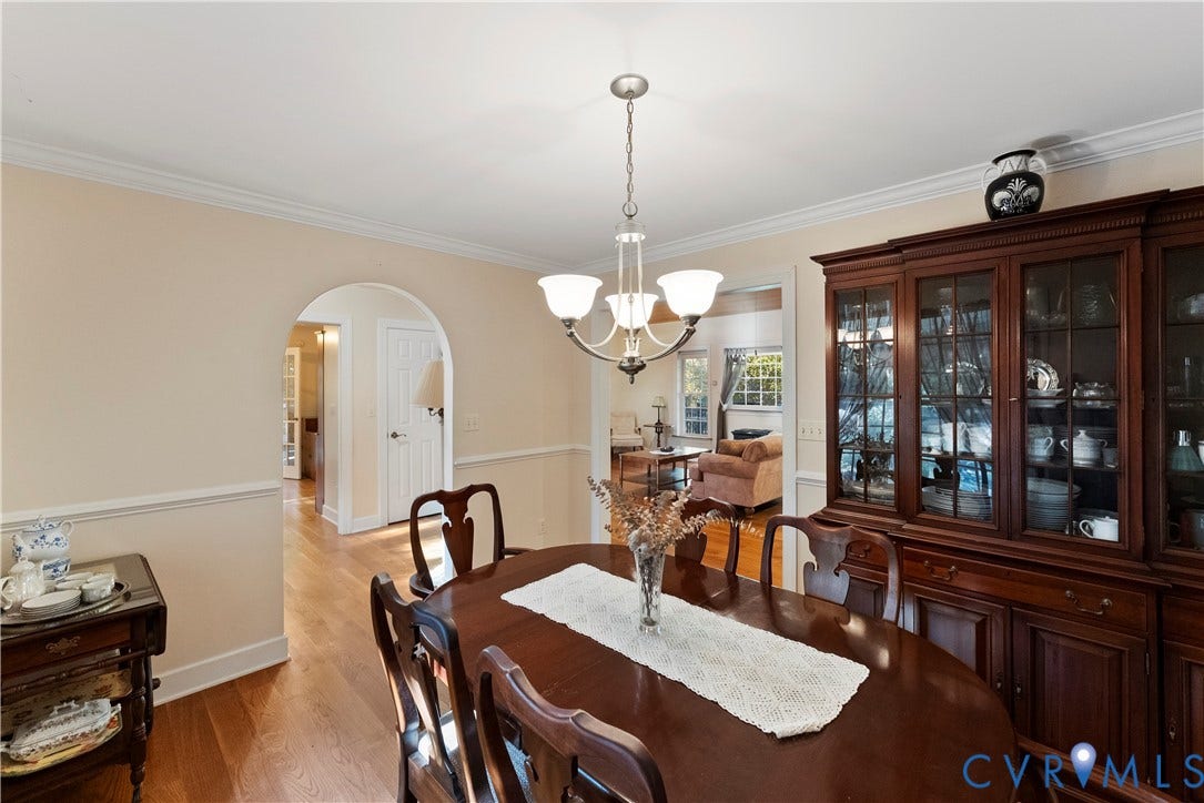 Dining space featuring wood-finish flooring, an arched doorway, crown molding, chair rail trim, and a multi-arm chandelier