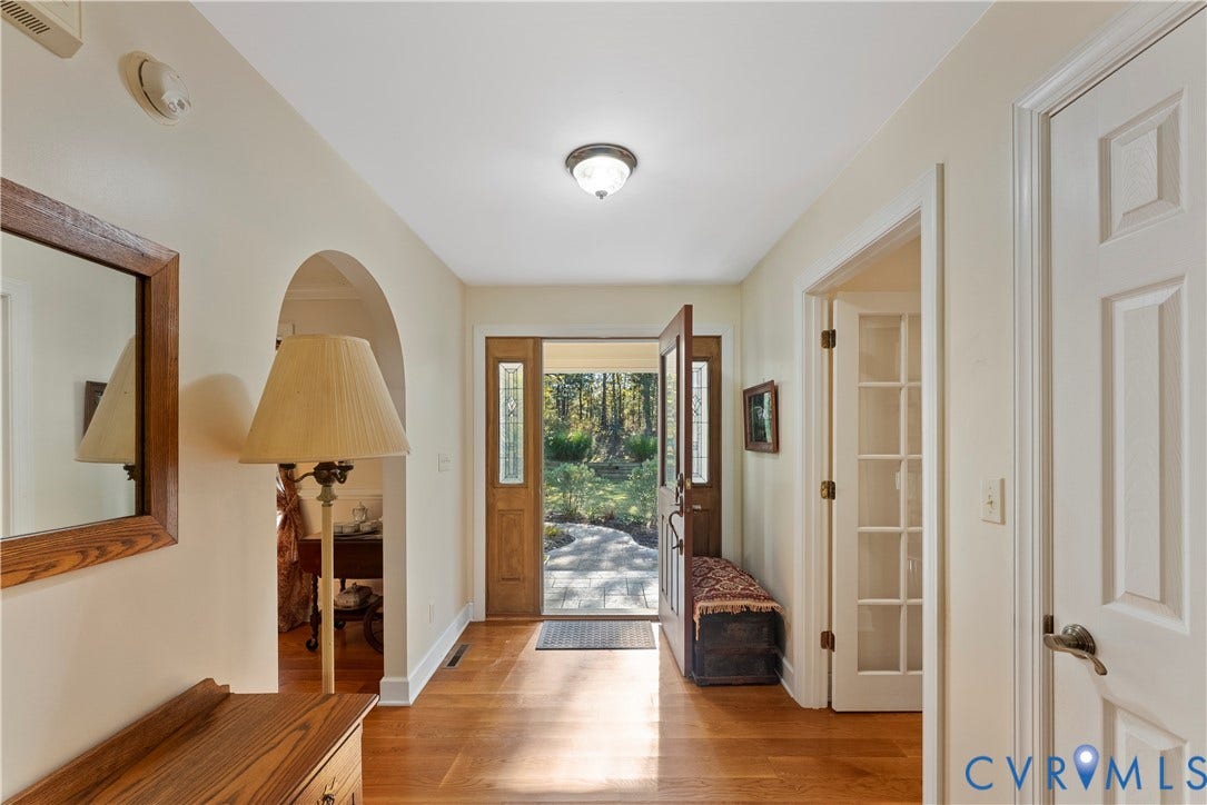 Foyer featuring wood-finish flooring, an arched architectural opening, and a natural wood-finish front door with glass sidelights