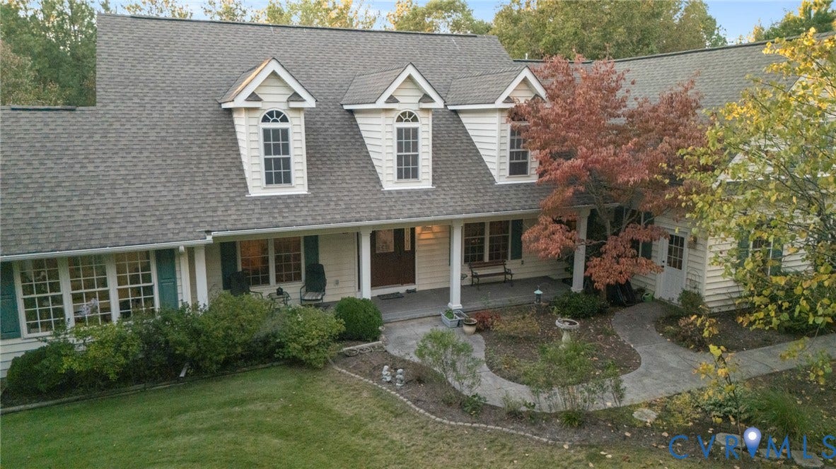 Multi-gabled exterior featuring horizontal siding, dormer windows, a covered front porch with round columns, and a paved stone walkway