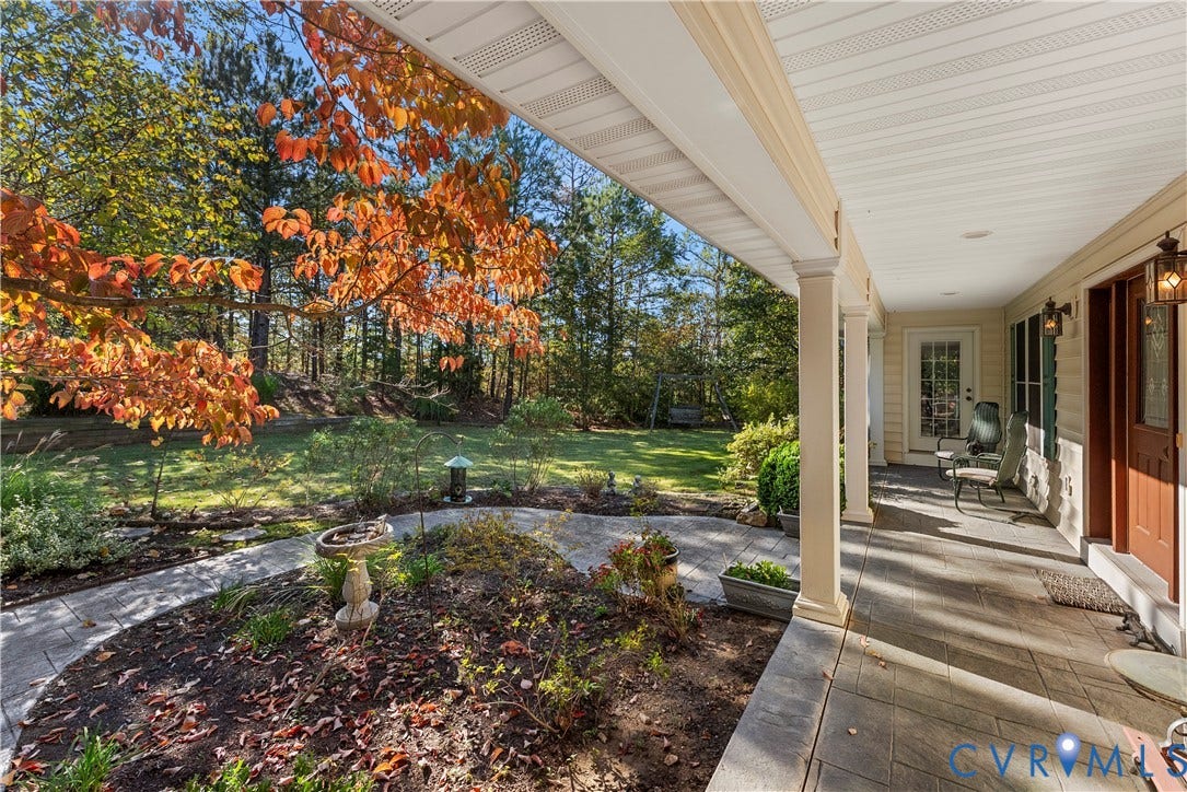 Covered porch featuring stone-tiled flooring, structural columns, and recessed lighting, transitioning to a stone walkway and a landscaped lawn area