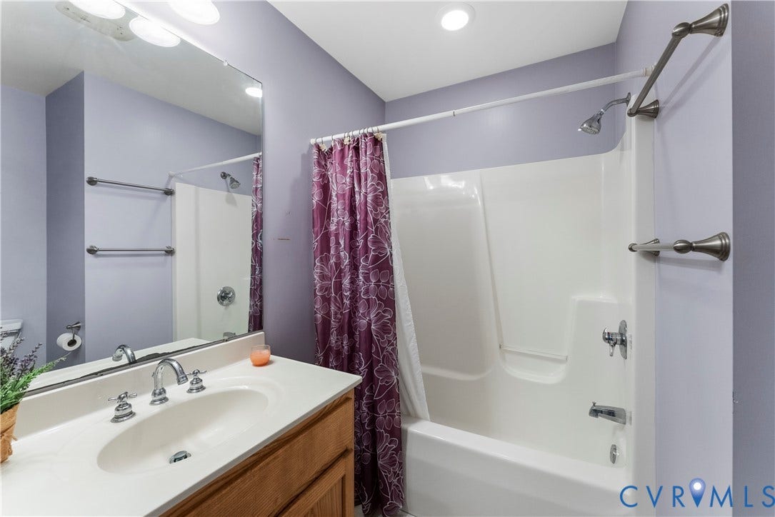 Bathroom featuring a wooden vanity, integrated basin, large wall-mounted mirror, and a combination bathtub and shower unit with a polished metal fixture