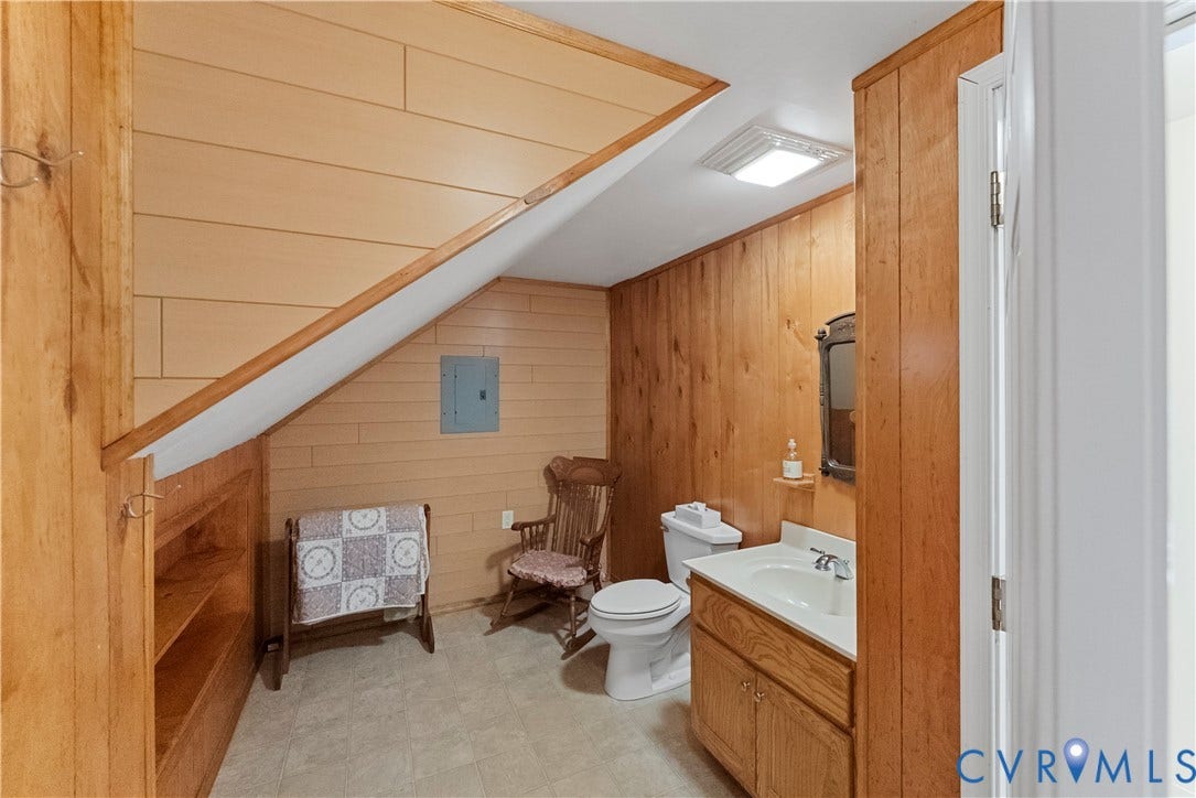 Bathroom featuring wood-paneled walls, built-in shelving, a porcelain toilet, and a vanity with a white countertop and integrated sink