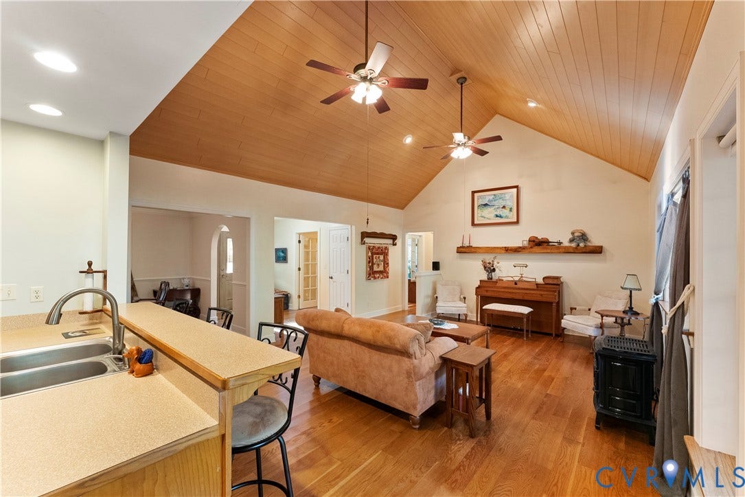 Vaulted wood-plank ceiling, wood-finish flooring, dual ceiling fans, and a rustic wood mantel