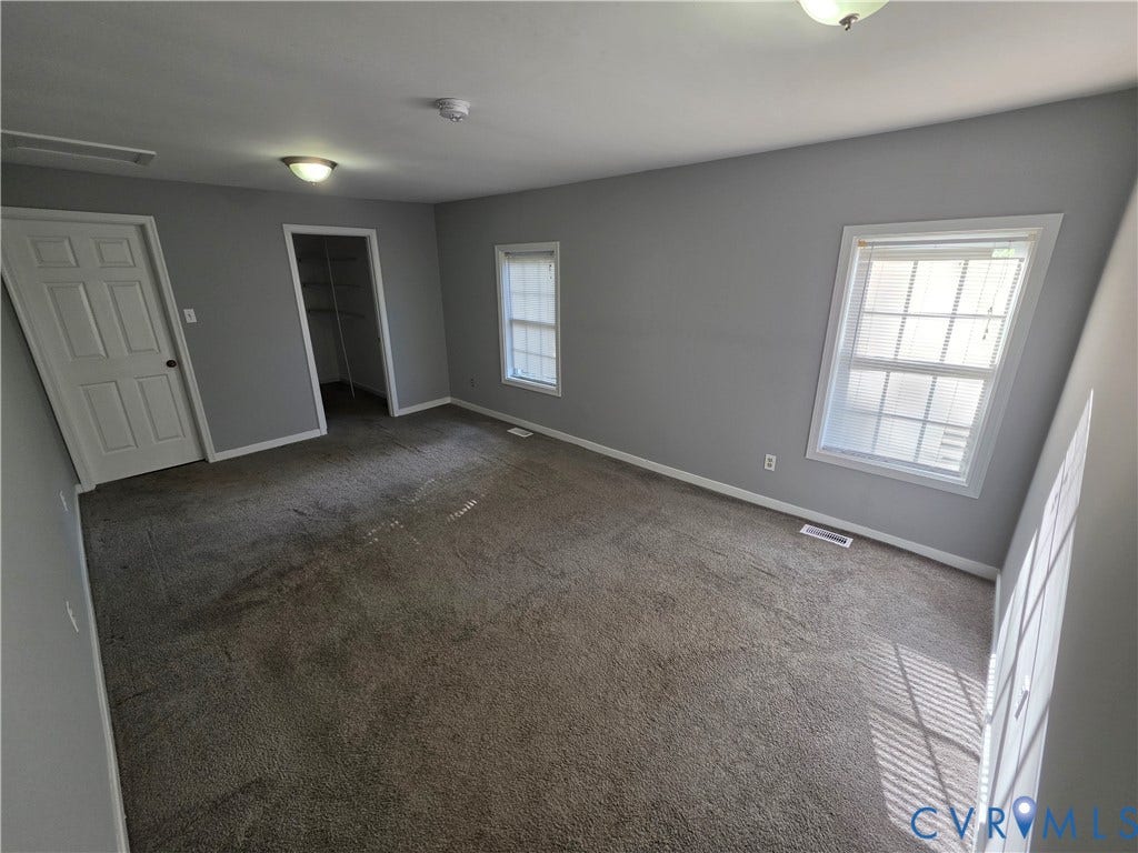 2406 Trenton Street, Hopewell, VA 23860 Neutral-toned room featuring wall-to-wall carpeting, two double-hung windows, and a walk-in closet with built-in shelving