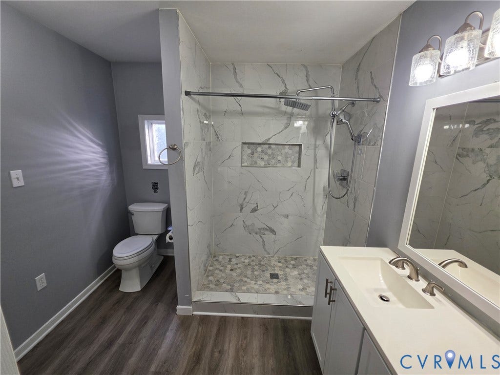 2406 Trenton Street, Hopewell, VA 23860 Bathroom featuring wood-finish flooring, a vanity with a white countertop and integrated sink, a walk-in shower with stone-tile surround, and a recessed shower niche