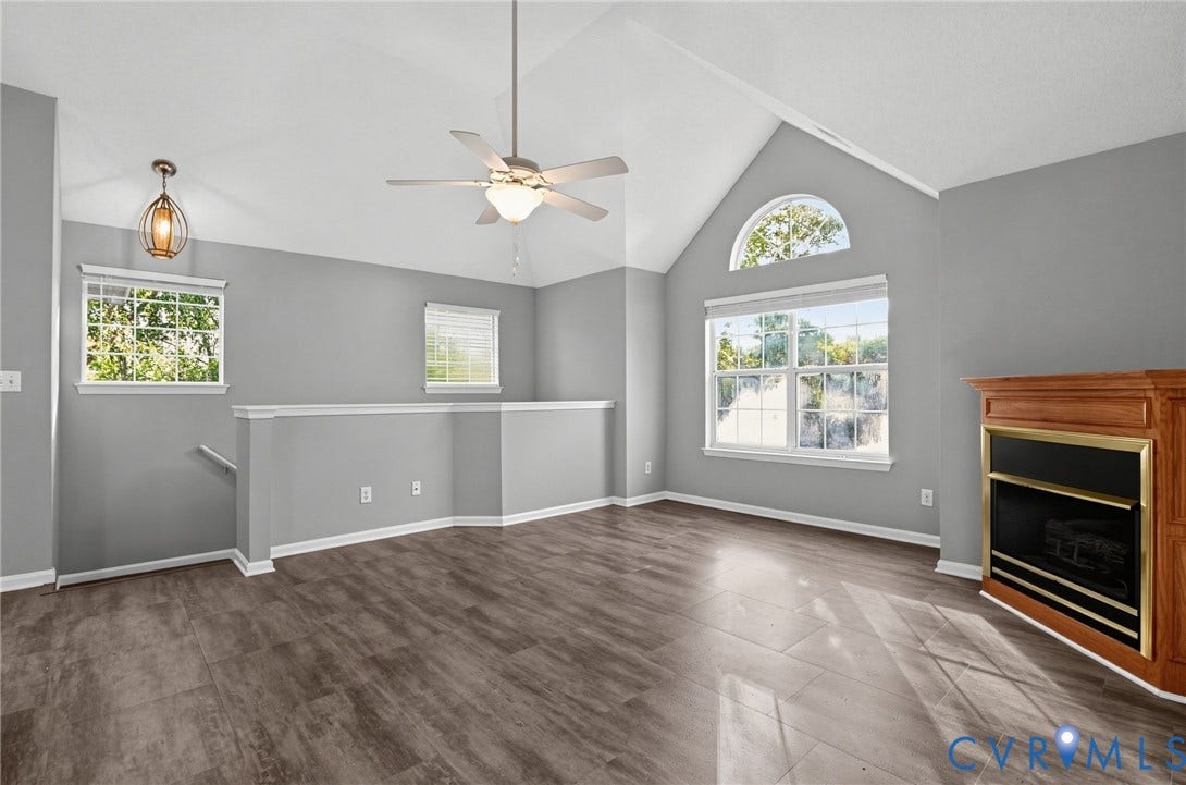 910 Rue Marseille, Les Chateaux, Chesapeake, VA 23320 Vaulted ceiling featuring an arched window, wood-finish flooring, fireplace with a wood mantel, ceiling fan with integrated lighting, and decorative pendant lighting