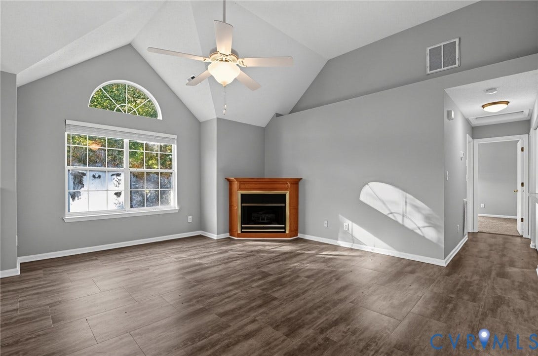 910 Rue Marseille, Les Chateaux, Chesapeake, VA 23320 Vaulted ceilings featuring an arched window, wood-finish flooring, and a corner fireplace with wood-tone surround and built-in ceiling fan