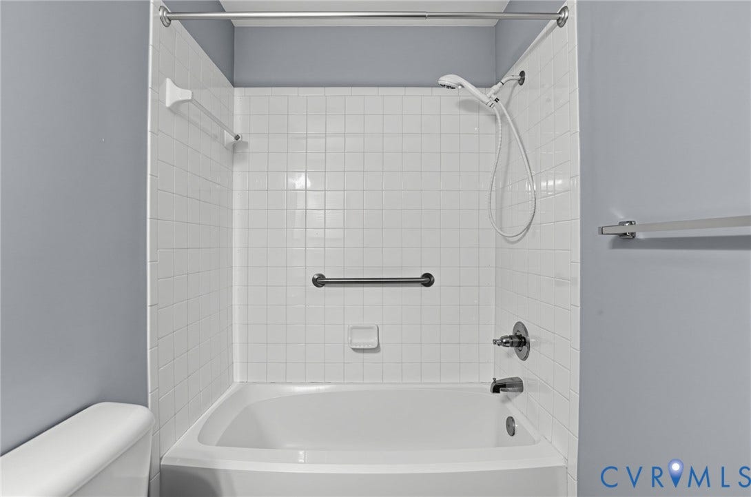910 Rue Marseille, Les Chateaux, Chesapeake, VA 23320 Bathtub surround featuring white square ceramic tile, handheld shower fixture, integrated grab bar, and wall-mounted metal towel bars