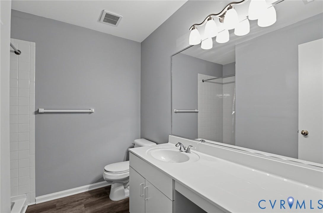 910 Rue Marseille, Les Chateaux, Chesapeake, VA 23320 Full-width vanity with integrated sink, expansive vanity mirror, multi-bulb overhead lighting, wood-finish flooring, and tiled shower surround