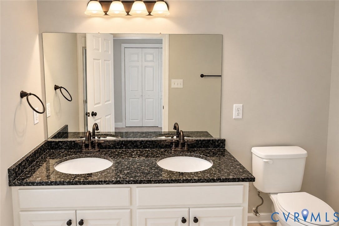 4229 Cedar Creek Lane, Prince George, VA 23875 Dual-sink vanity with a stone countertop, white cabinetry, polished metal fixtures, and a wall-mounted light fixture