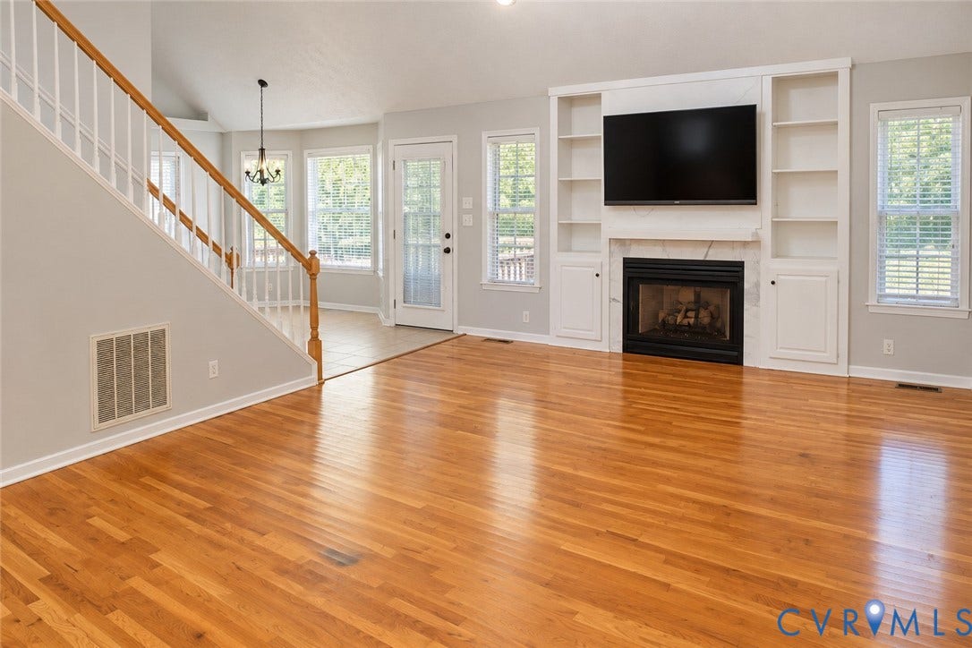 4229 Cedar Creek Lane, Prince George, VA 23875 Open-concept living space featuring wood-finish flooring, vaulted ceilings, a fireplace with floor-to-ceiling built-in shelving, and a wood-railing staircase