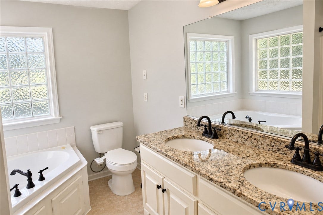 4229 Cedar Creek Lane, Prince George, VA 23875 Dual-sink vanity with stone countertop and matte black fixtures, jetted soaking tub with tile surround, and privacy-glass windows