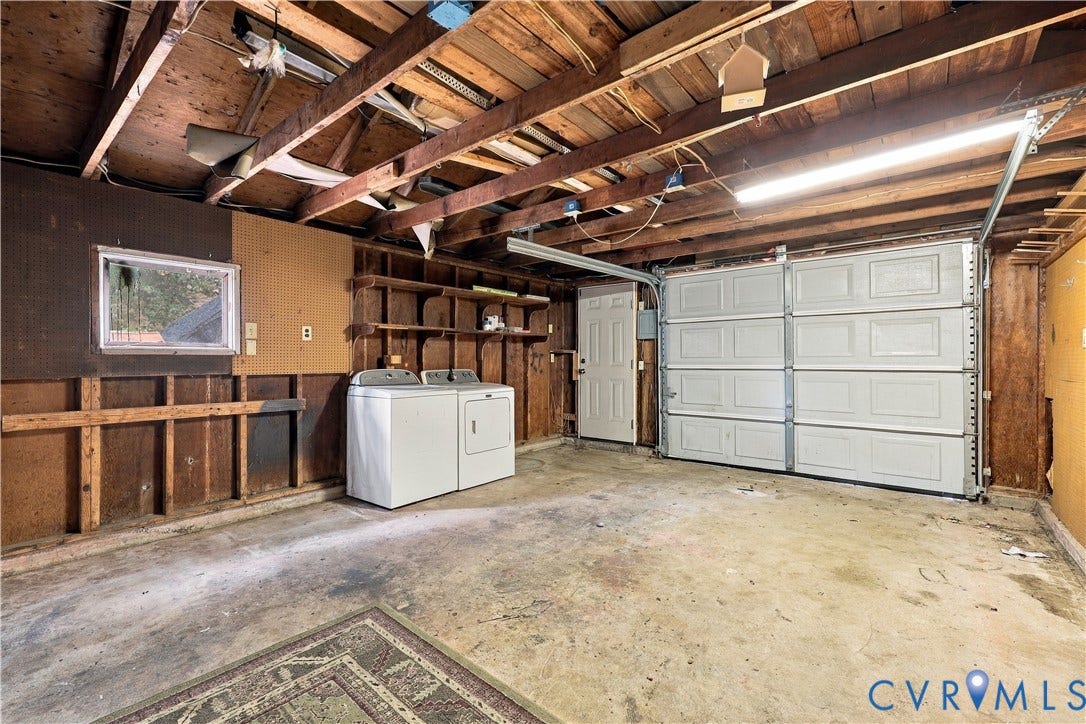 305 Arizona Street, Kingman Heights, Portsmouth, VA 23701 Garage space featuring exposed timber ceiling joists, panelled wood-finish wall detailing, integrated wall-mounted shelving, a sectional roll-up door, and laundry hookups