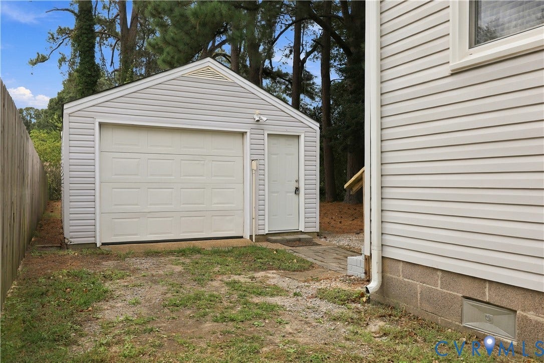 305 Arizona Street, Kingman Heights, Portsmouth, VA 23701 Detached single-car garage featuring light-colored vinyl siding, a white roll-up garage door, a side entry door, and a concrete block foundation