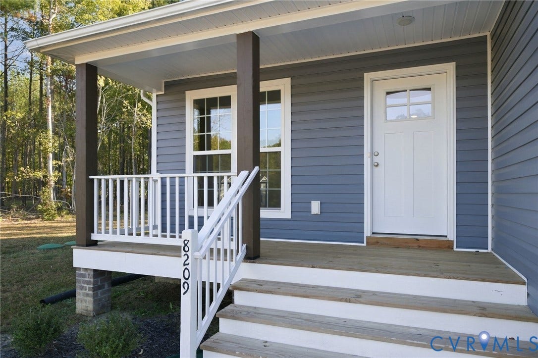 8209 Grantham Woods Way, Grantham Woods, Henrico, VA 23231 Covered front porch featuring wood-finish decking, white railings, dark-tone support posts, and a white six-panel door with glass inlay