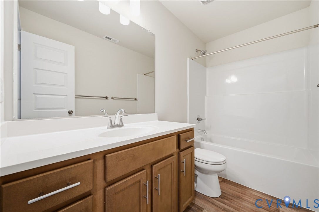 8209 Grantham Woods Way, Grantham Woods, Henrico, VA 23231 Bathroom featuring wood-finish cabinetry, a large integrated countertop vanity, full-width mirror, and a tub-shower combination with surround