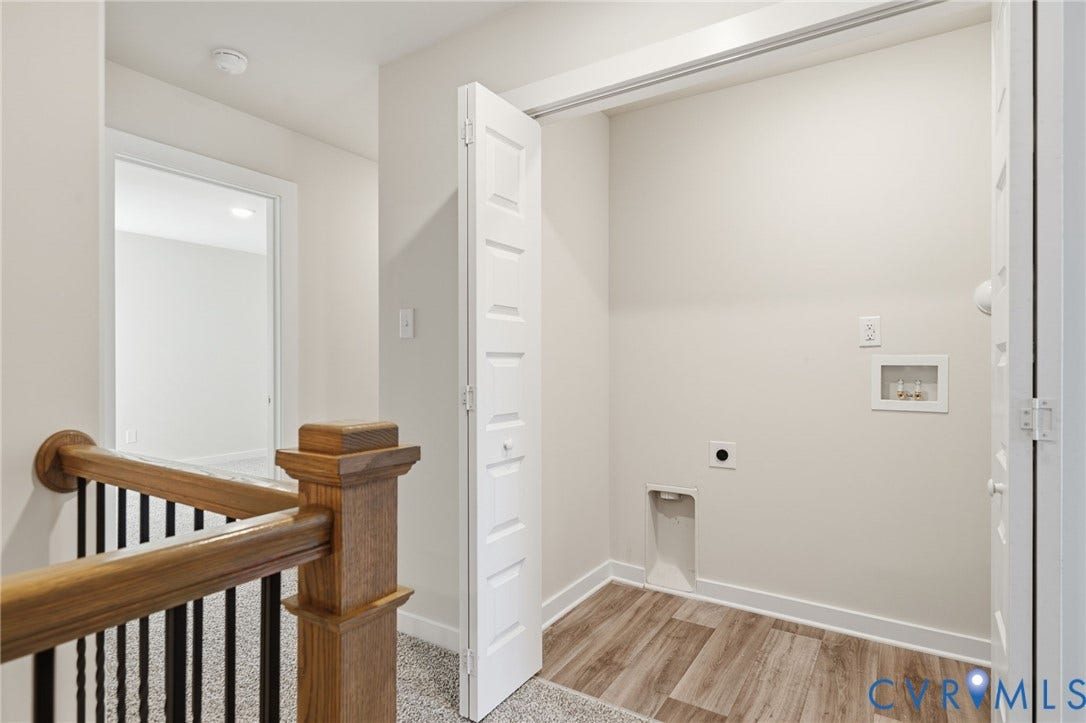 8209 Grantham Woods Way, Grantham Woods, Henrico, VA 23231 Laundry closet featuring wood-finish flooring, white bi-fold doors, and integrated utility hookups, complemented by wood-finish handrail and black metal balusters