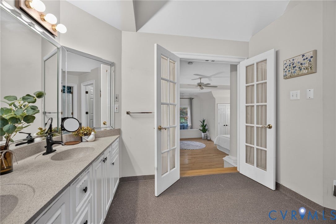 Double vanity with integrated sinks, neutral solid-surface countertops, multi-light vanity fixtures, and double glass-paneled French doors