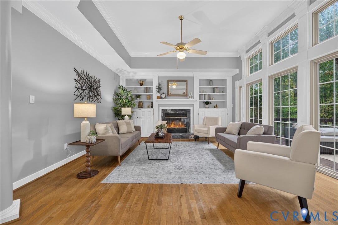 Living room featuring wood-finish flooring, floor-to-ceiling windows, crown molding, built-in shelving, and a fireplace with stone surround