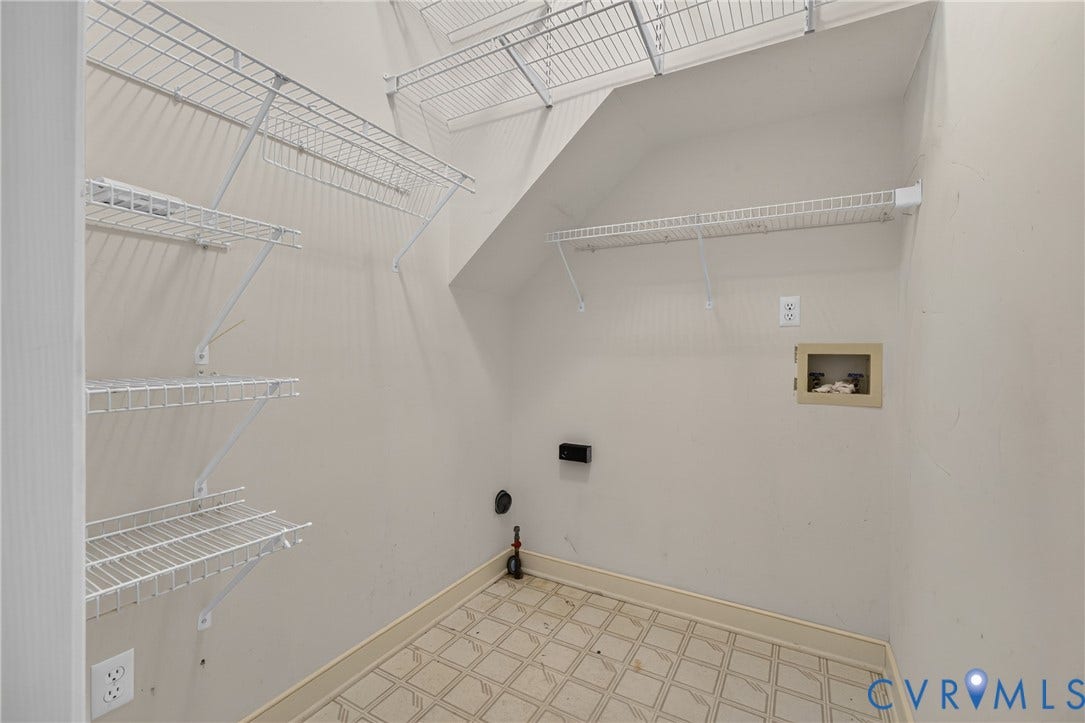 Storage area featuring tiered white wire shelving, a grid-patterned floor, and integrated wall-mounted utility connections