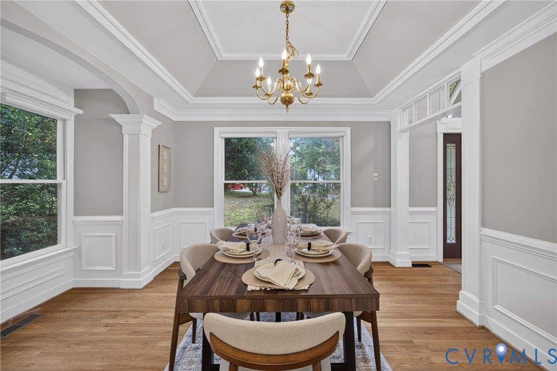Tray ceiling with crown molding, wainscoting, wood-finish flooring, and brass-finish chandelier