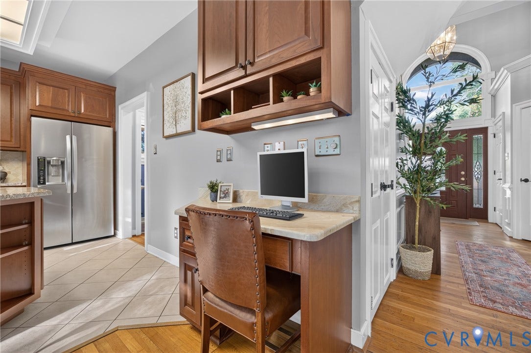 Built-in desk area with stone countertop, upper cabinetry with open shelving, stainless steel refrigerator, tile and wood-finish flooring, and arched entryway featuring decorative door glass