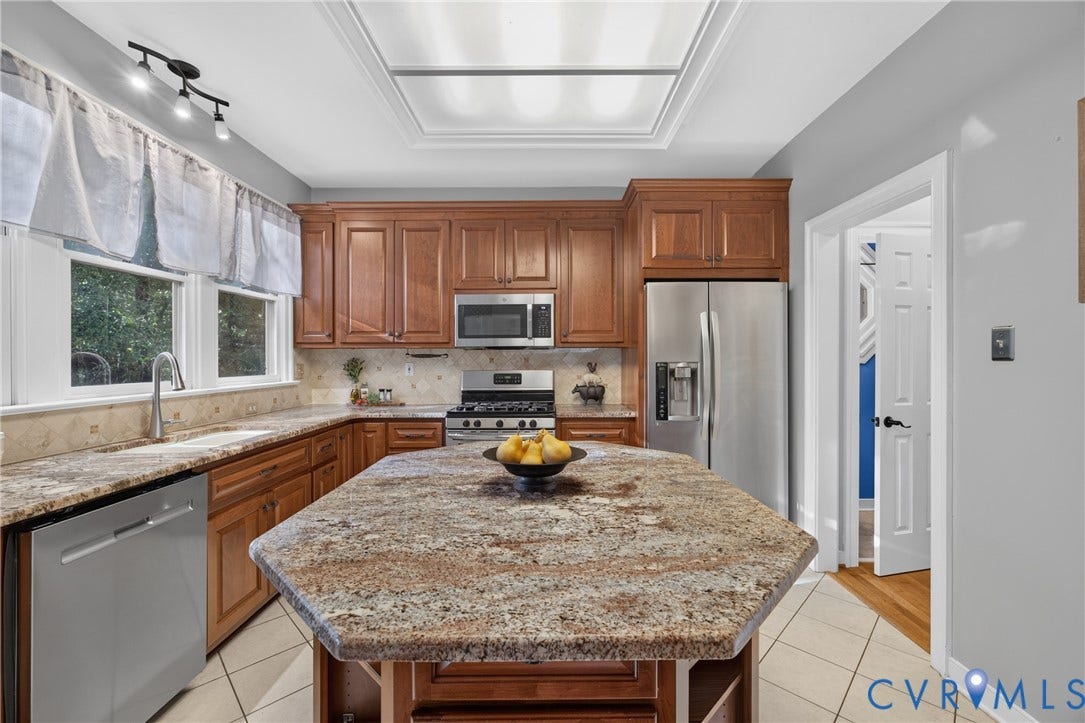 Kitchen featuring a central island with a stone countertop, stained wood cabinetry, stainless steel appliances, recessed ceiling lighting, and tile flooring