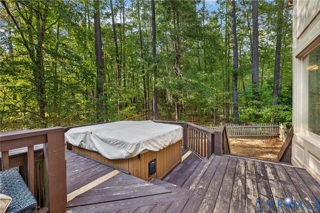 Multi-level wood deck featuring a built-in hot tub, wood railings, and a picket fence enclosure