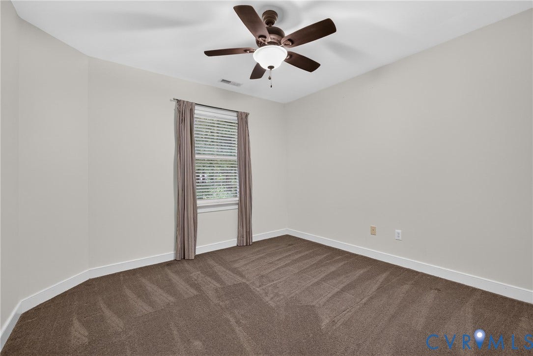 Neutral-toned interior featuring wall-to-wall carpeting, a multi-blade ceiling fan with an integrated light fixture, and a single-hung window