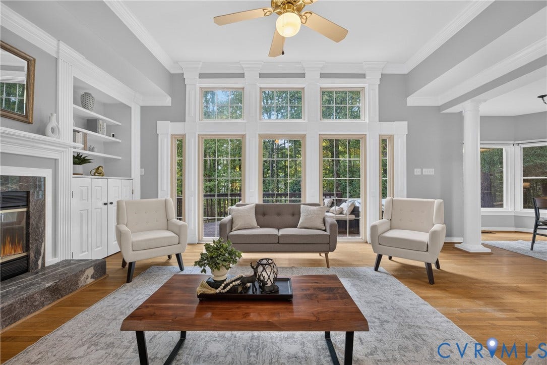 Vaulted ceilings featuring crown molding, floor-to-ceiling windows with grid detailing, built-in shelving, stone-surround fireplace, and wood-finish flooring