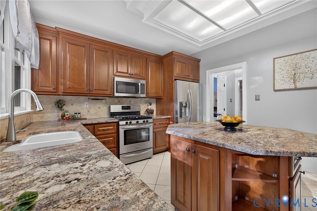 Kitchen featuring natural wood cabinetry, stone-surface countertops, stainless steel appliances, a central island with integrated shelving, and recessed ceiling lighting