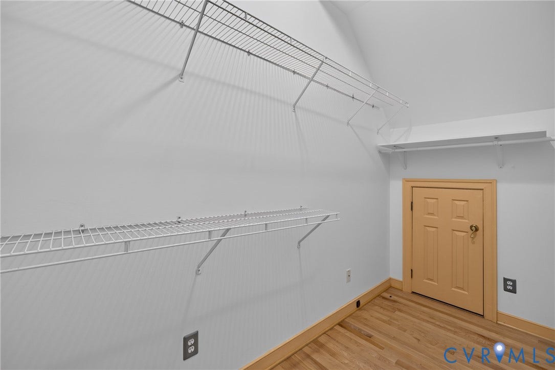 Storage area featuring wood-finish flooring, white walls, tiered wire shelving, and a natural wood-trim access door