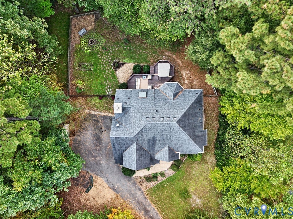 Aerial perspective of a multi-gabled roofline with a chimney, featuring an expansive wooded lot, a multi-level deck, and a stone-paver walkway