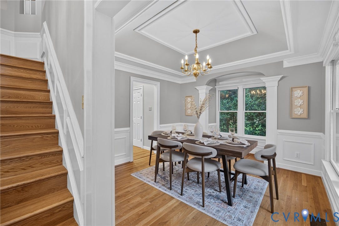 Dining area featuring a tray ceiling with crown molding, wainscoting, wood-finish flooring, a multi-arm chandelier, and a wood-finish staircase with white handrails