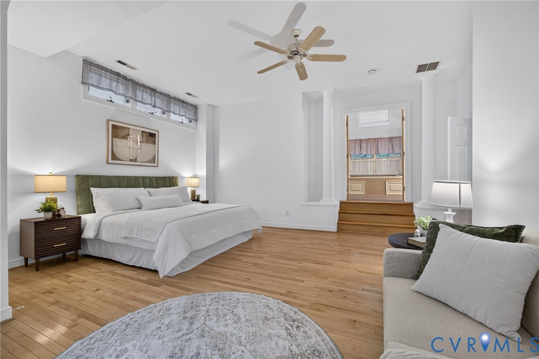 Expansive room featuring wood-finish flooring, high ceilings with a central paddle fan, elevated entry with decorative columns, and a wide clerestory window