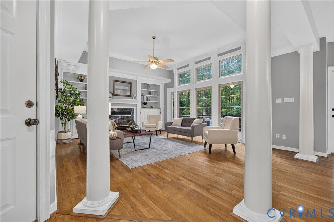Living area featuring wood-finish flooring, floor-to-ceiling windows, dual decorative columns, and built-in shelving flanking a fireplace