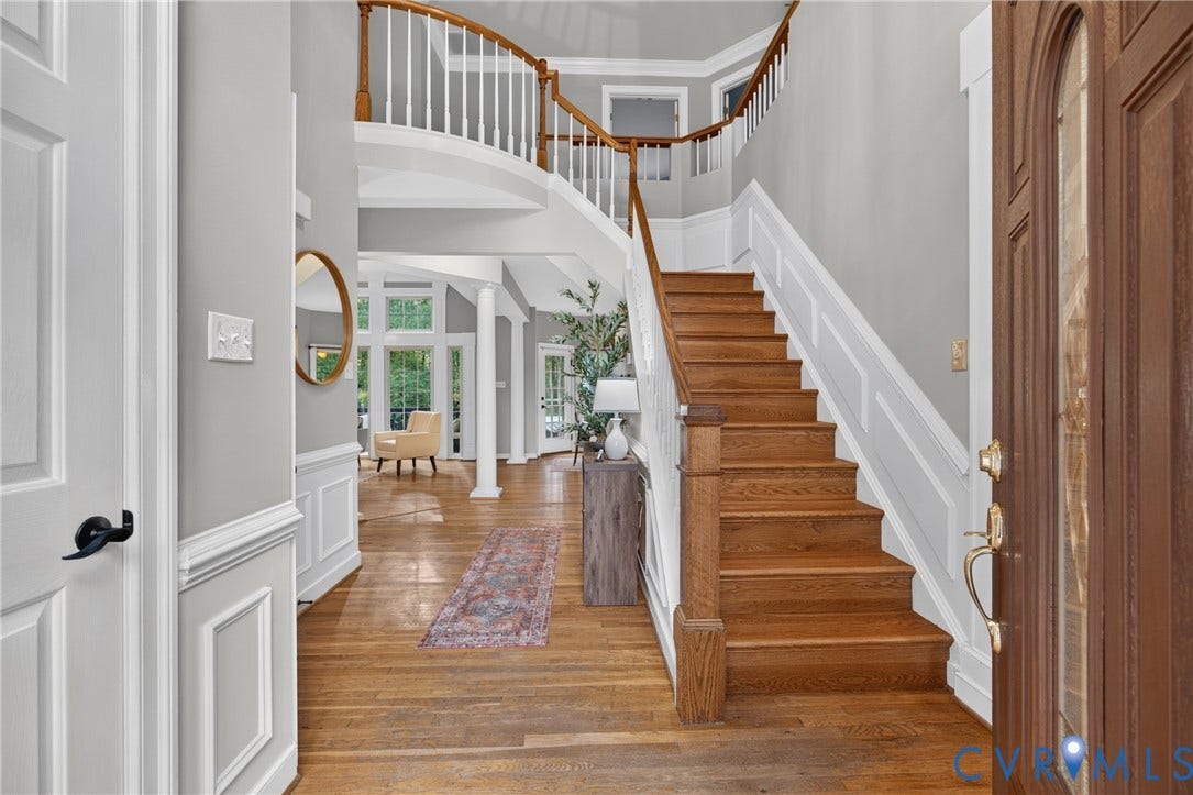 Grand foyer featuring a wood-finish staircase with decorative balusters, wood-finish flooring, wainscoting, and a curved landing