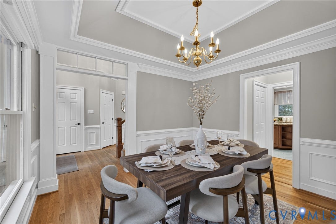 Dining area featuring wood-finish flooring, crisp white wainscoting, a tray ceiling, and a traditional brass chandelier