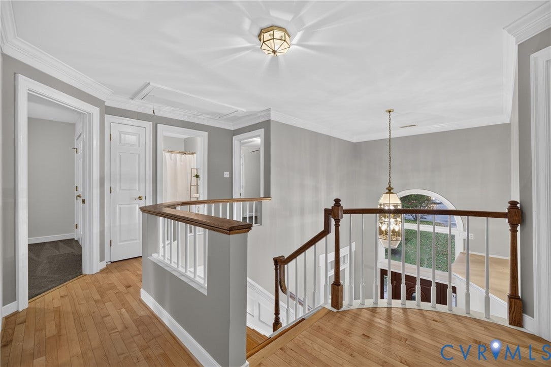Landing featuring wood-finish flooring, a wood-topped railing with white balusters, crown molding, and a suspended multi-tiered chandelier