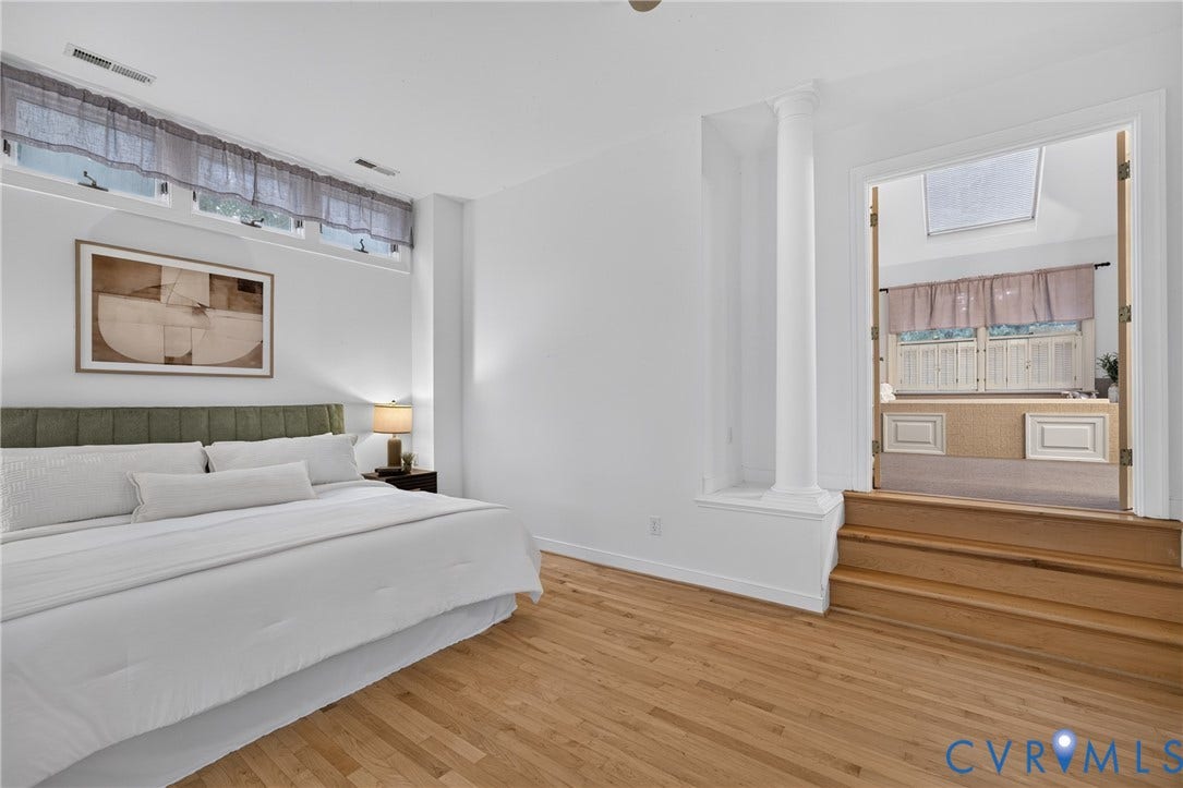 Room featuring wood-finish flooring, clerestory windows, a decorative column, and a raised platform entry with double doors