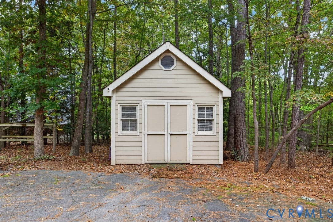 Detached storage structure featuring horizontal siding, double entry doors, dual windows, and an octagonal gable vent, situated on a paved surface
