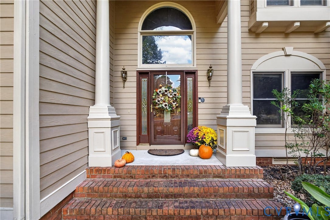 Front entryway featuring a brick staircase, dual structural columns, arched transom window, and paneled wood door with glass sidelights