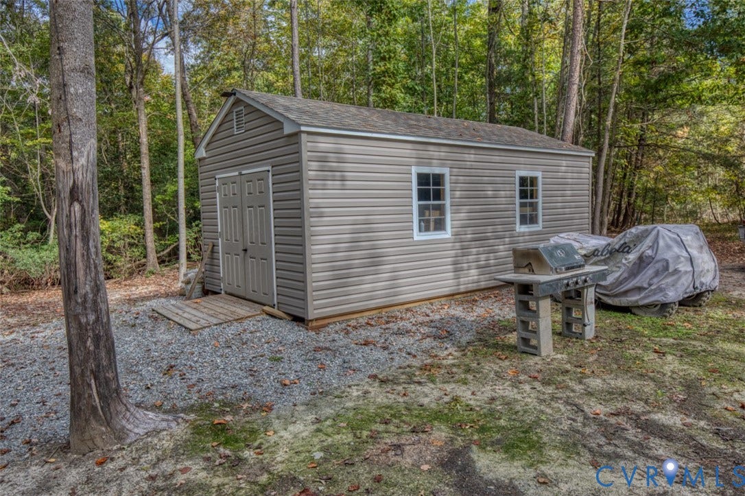 13501 Cooks Mill Court, Cooks Mill, Lanexa, VA 23089 Detached storage structure featuring horizontal vinyl siding, a gabled roof, dual-entry doors, and multi-pane windows, situated on a gravel pad